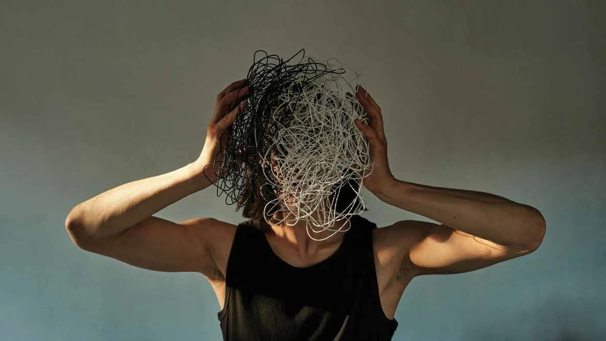 A person holding a tangled mass of threads in front of their face